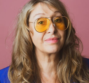 Foto von Vera Dreyer mit gelber Brille und rosa Hintergrund